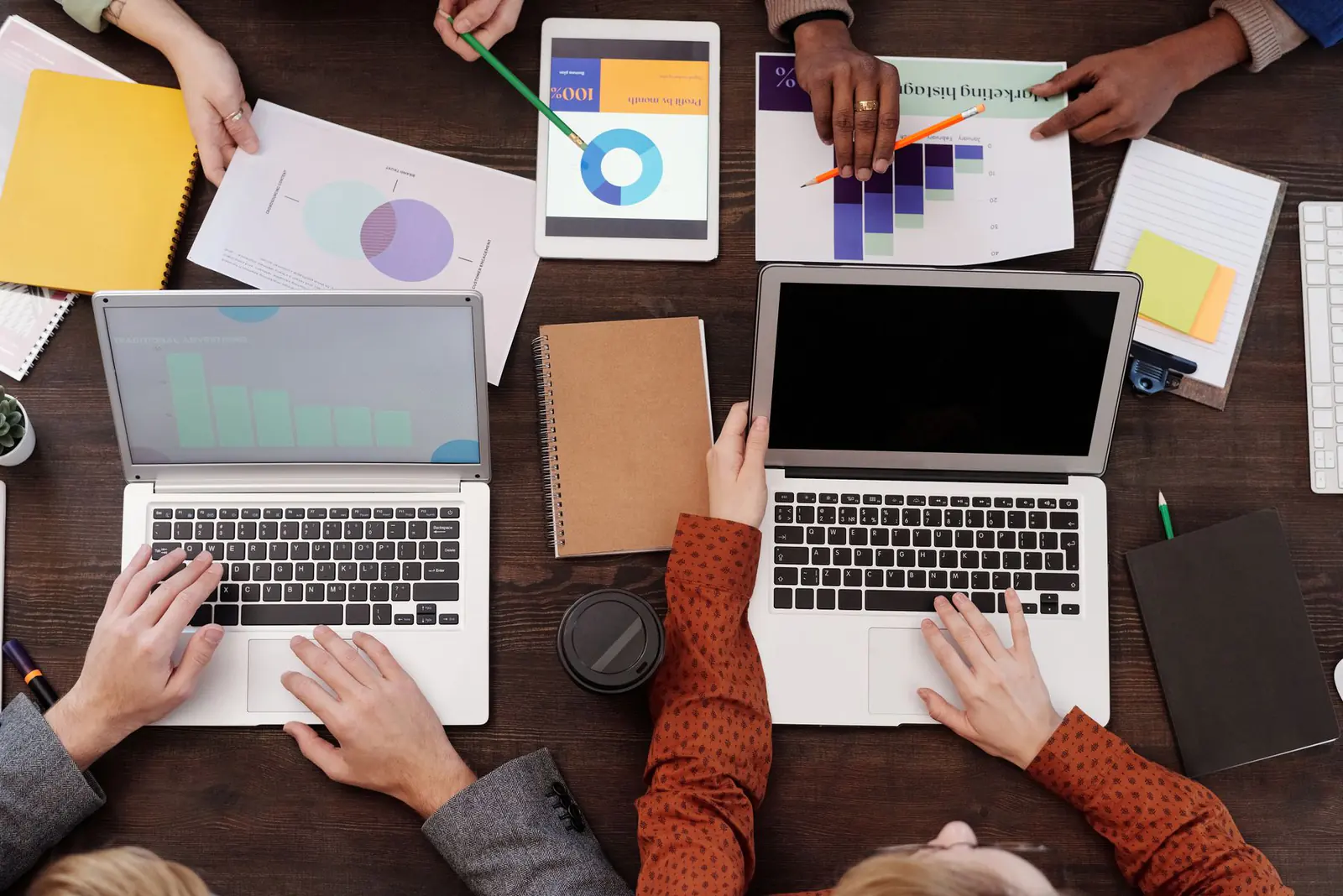 Two laptops, notebooks and printed charts on a desk, seen from above