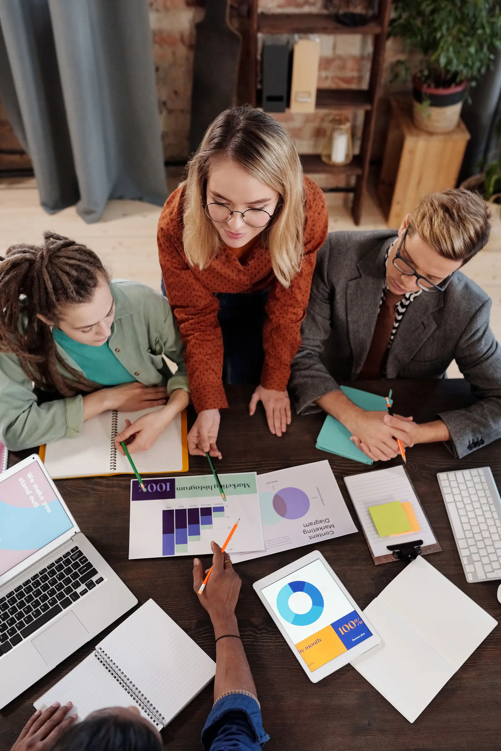 Three people leaning over a desk of laptops and charts